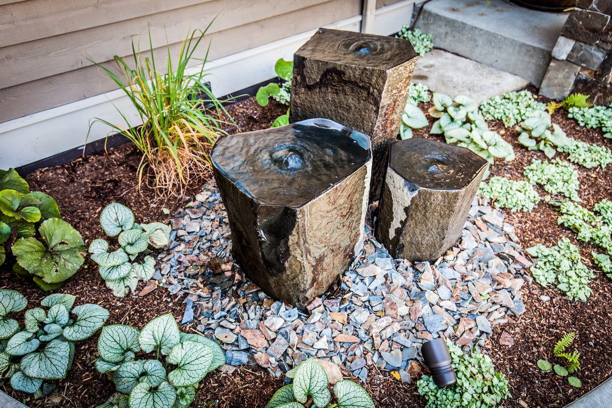 fountain in landscape bed surrounded by plantings and stone