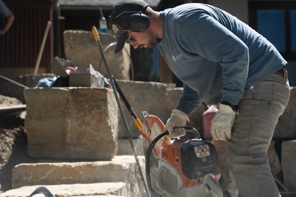 landscape installation crew member cuts stone 