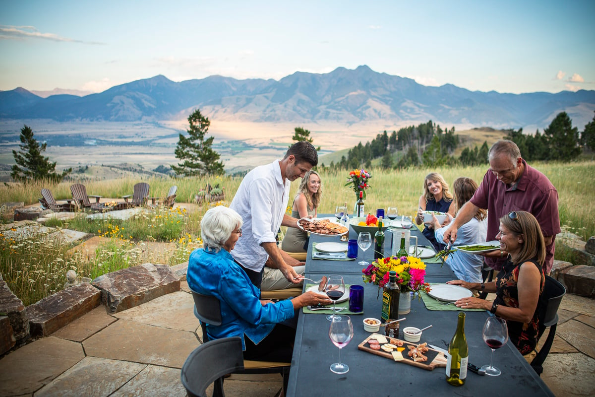 family sits at table for dinner on flagstone patio with view of mountains